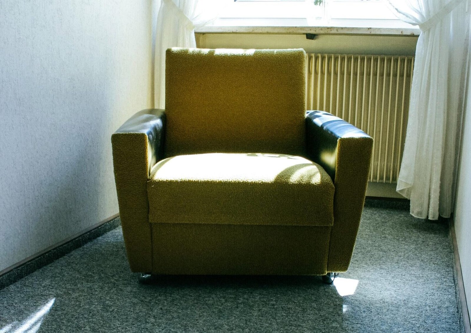 Minimalist interior featuring a cozy armchair and flower vase by a sunlit window.